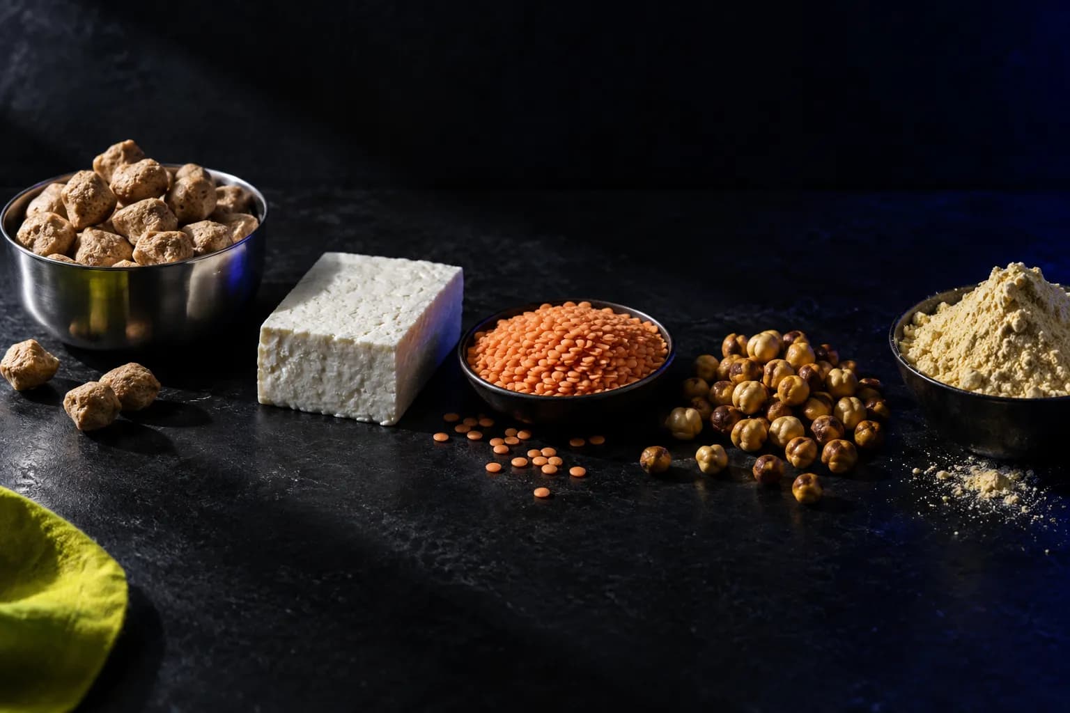 Soya chunks, paneer, dal, chana and besan laid out on near-black beside a lime cloth.